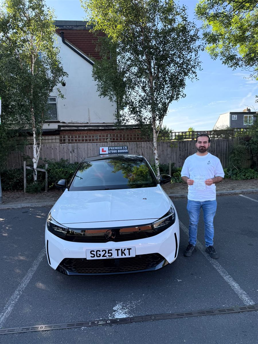 Learner showing his practical driving test pass certificate next to the school car
