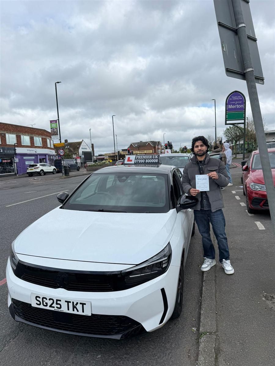 Learner holding up his test pass certificate next to the driving school car
